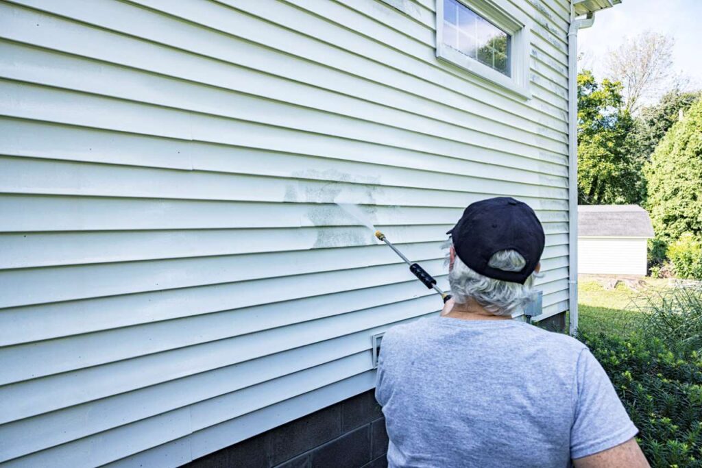 homeowner is cleaning the vinyl siding on her house with high pressure washer
